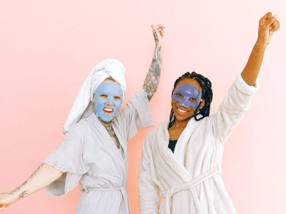 Content multiracial female friends in cosmetic masks raising hands